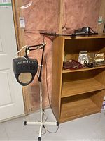 Wider view showing the taller black magnifying lamp mounted on a white wheeled stand next to a wooden bookshelf, with power cord visible.
