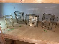 Four miniature glass display cases with brass trim on a wooden surface, one shows visible cracks on the top glass panel.