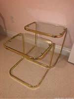 Angled side view of the pair of nesting tables showing gold-tone metal tubular frames and glass tops