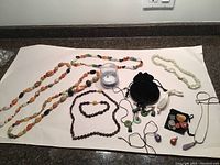 Wide view of assorted necklaces, bracelets, pendants and loose polished stones arranged on white paper