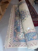 Rolled patterned area rug showing floral and geometric border design with fringe.