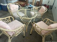 View of four rattan chairs with pink cushions arranged around the glass top rattan table.