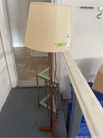 Photo showing the retro floor lamp with teak-look wooden stand and cream lampshade, placed near the triangular metal framed table.