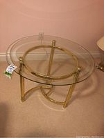 Side view of the round side table showing the metal base and circular glass top with beveled edges.