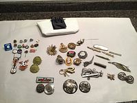 Full lots layout showing assorted vintage brooches and pins with some badges, a clutch or small purse and embroidered patch