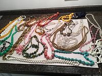 Wide view showing 22 vintage bobble and beaded necklaces in assorted materials and colors laid out on counter.