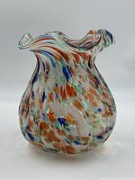Front and side views of a colorful antique art glass vase. The vase has a ruffled clear top with swirled colorful spots in orange, blue, green, and white throughout the body.