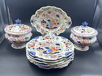 Two lidded bowls flanking stack of five dessert plates with scalloped oval platter at back