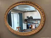 Full view of the oval mirror mounted on wall reflecting interior kitchen and dining room.