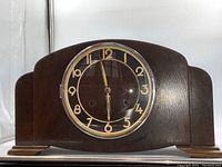 Front view of the antique wooden mantle clock showing the clock face with gold Arabic numerals and hands and the wooden casing.