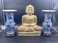 Front view of Buddha statue centered between two blue and white porcelain vases with stands