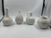 Full view of 4 white porcelain vases with gold accents and one matte white embossed vase with handle