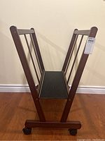 Front view showing the V-shaped mahogany stained frame with black bottom shelf and four caster wheels.