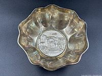 Top-down view of silver bowl showing scalloped edge and central medallion with medieval village scene.