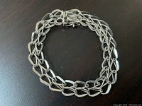 Close-up view of full bracelet coiled on dark surface showing link design and clasp.