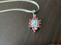 Close-up of pendant front showing opal center and surrounding red stones, chain partially visible on dark background