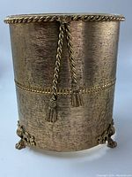 Front view showing gold gilt metal textured surface with rope and tassel design and claw feet.