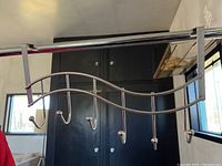 Front view of silver metal towel rack with wave design and six hooks, hanging on a black cabinet.