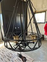 Photo of two-light chandelier showing black cage frame and gold bulb sockets, with loose wiring visible inside and below the fixture.