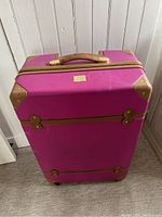 Full front view of the large DVF Studio luggage, showing hot pink exterior and tan trim with gold accents.