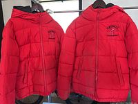 Two Fireball Whiskey branded red puffer jackets hung side by side showing front zipper closures and logo placement.
