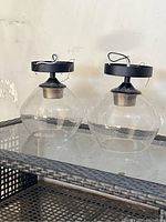Pair of flush mount ceiling lights placed on a glass table with woven base. Clear square-shaped glass shades. Black circular ceiling mounts with wiring visible.