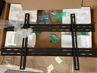 Photo showing the black metal flush TV mount bracket laid out with remaining mounting hardware in packaging.