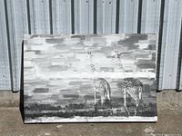 Front view of black and white giraffe canvas art depicting two giraffes on grassy plains with a patchy cloudy sky background.