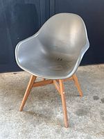 Full view of a gray molded plastic chair with wooden legs on a concrete floor, showing wear and dirt.