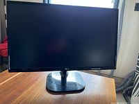 Front view of LG computer monitor placed on a wooden table, screen black and bezel thin