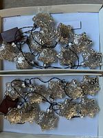 Two sets of mercury glass snowflake-shaped Christmas lights laid out in their boxes showing the bulbs and battery compartments