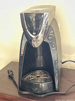 Front view of black Mr Coffee branded coffee machine with chrome accents, showing power and brew buttons, drip tray, and pod holder area.