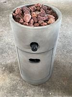 Gray cylindrical propane patio fire pit with lava rocks on top and a black control knob on the side.