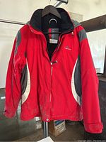 Full view of the red, grey, and white Rossignol ski jacket on a hanger showing wear and dirt marks.