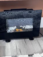 Front view of the small electric fireplace heater showing black glass exterior and clear crystal embers inside.