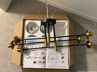 Partially assembled black and gold Sputnik chandelier laid on cardboard with assembly instructions underneath.