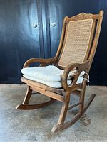 Front and side view of wooden rocking chair with cane backrest and cushion on the seat.