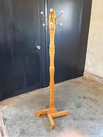 Full view of the tall wooden coat rack showing four metal hooks with white tips and ornate wood pole.