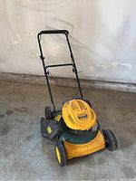 Yellow and green Yard Man push lawn mower with black handle, showing overall condition and structure.