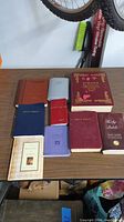 View of all nine religious books arranged on a wooden table including Bibles, prayer book, and dictionary of Bible themes.