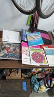 Photo showing binders, adult coloring books, sketchbook and some crafting supplies on a table.
