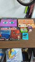 Photo showing Monopoly Spider-Man edition board game, True Colors board game, Cat-opoly, and several small card games on a table.