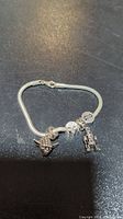 Photo of entire silver bracelet with Yoda, Rebel Alliance symbol, and R2-D2 charms laid against black background.