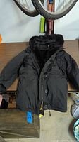 Black winter coat laid flat on a surface showing fur-lined hood and button/zipper front
