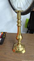 Front view of tall brass candlestick holder showing curved shaft and hexagonal base.