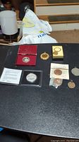 Coins spread on a black surface showing silver American Eagle coin in red box, certificate and other coins including pendants and wrapped pieces