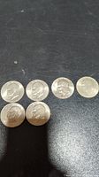 Top and front view of six Eisenhower dollar coins laid out on a black surface.