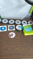 Photo of multiple software discs laid out on wooden surface including QuickBooks boxed software and various other CDs, some in sleeves and some loose