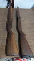 Two wooden M1 rifle stocks placed side by side on a wooden surface showing general shape and wear.