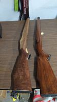 Two Mauser rifle stocks laid side by side on a table, showing the front and sides. One stock with heavy wood damage on forend.